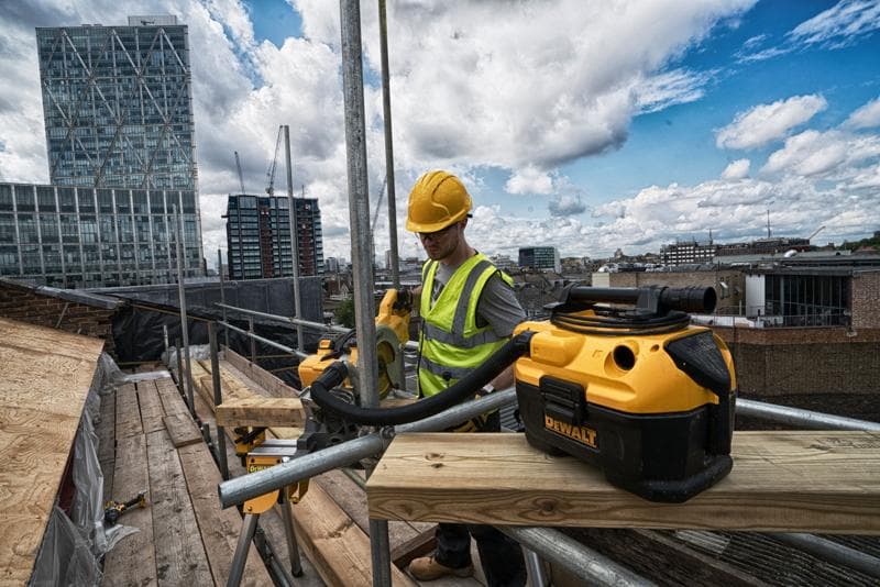 Aspirador DEWALT DCV584 em obra no telhado com trabalhador e prédios urbanos ao fundo.
