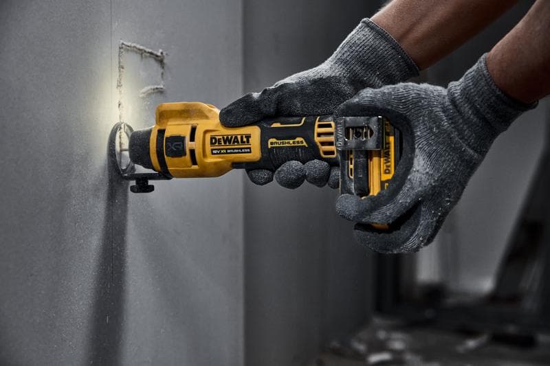 Ferramenta rotativa sem fio DEWALT cortando drywall, operada por mãos com luvas.