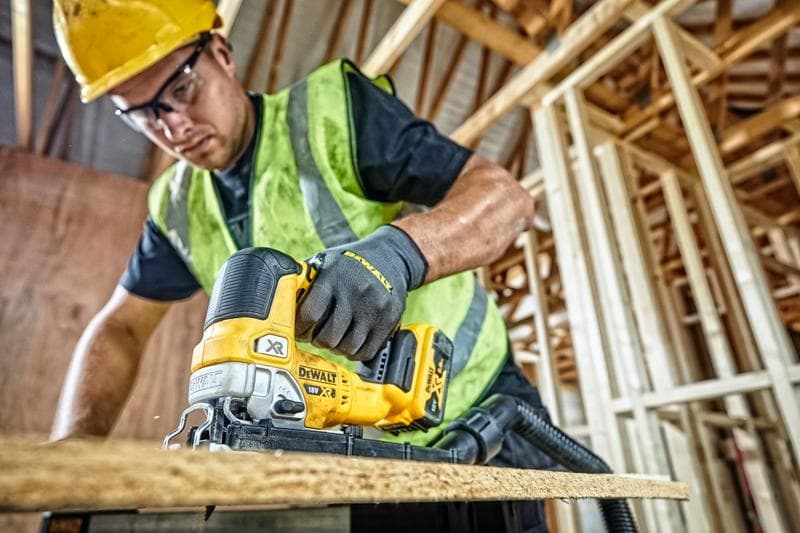 Serra DEWALT DCS334P2 usada para cortar madeira em obra, operador com equipamentos de segurança.