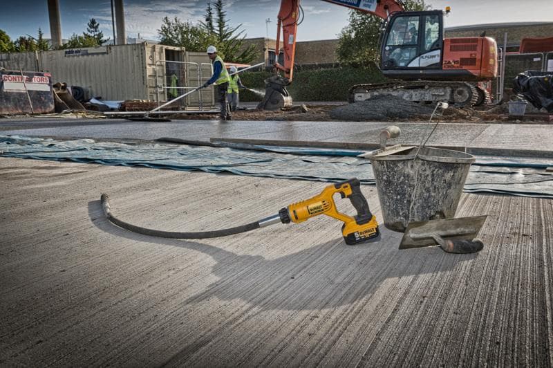 Uma ferramenta vibradora de concreto DEWALT DCE531N está colocada em um canteiro de obras, ao lado de um balde de metal e