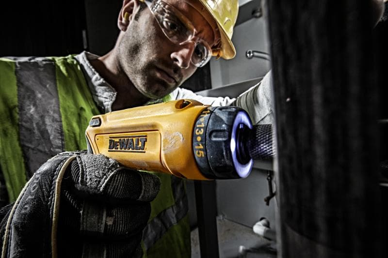 Pessoa usa chave de fenda DEWALT DCF680G2 amarela com luva em ambiente industrial.