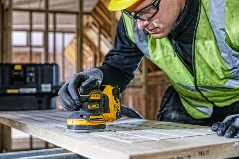 DEWALT DCW210, DCW210D1 lixadeira usada na madeira, obra, pessoa com luvas e colete de segurança.