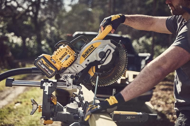 Pessoa corta madeira ao ar livre com uma serra de esquadria DEWALT sem fio; ferramenta amarela-preta XR FLEXVOLT.