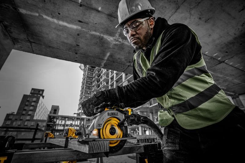 Pessoa usa serra circular DEWALT DCS565NT em obra, com equipamento de segurança, cortando madeira.
