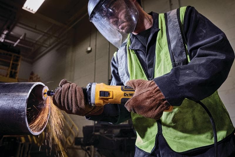 Trabalhador usa esmerilhadeira DEWALT cortando tubo metálico, faíscas, com luvas e equipamentos de proteção.