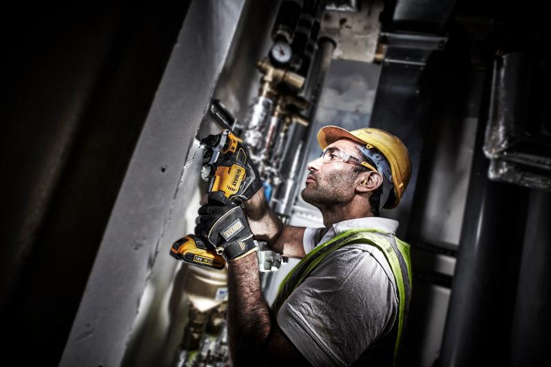 Trabalhador usa a ferramenta DEWALT DCS355D2 na parede, com equipamento de segurança e luvas.
