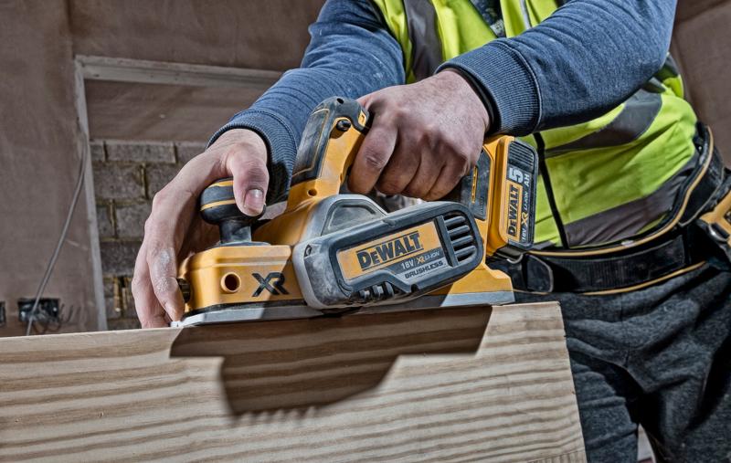 Pessoa usando uma plaina sem fio DEWALT DCP580N em madeira em um canteiro de obras.