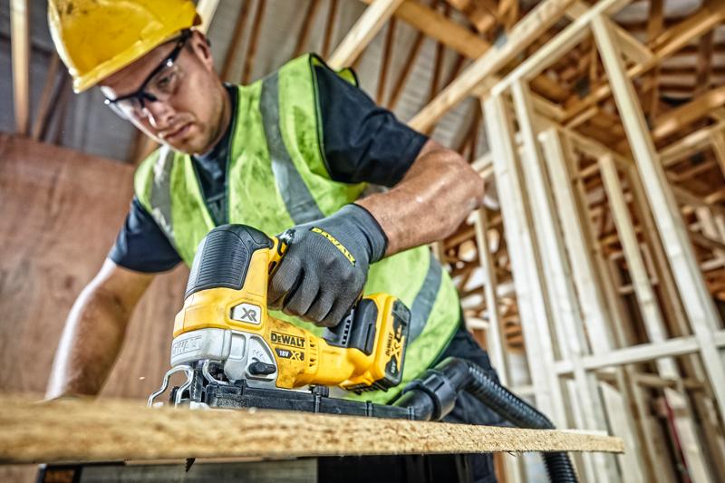 Serra DEWALT DCS334P2 usada para cortar madeira em obra, operador com equipamentos de segurança.