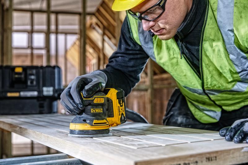 DEWALT DCW210, DCW210D1 lixadeira usada na madeira, obra, pessoa com luvas e colete de segurança.