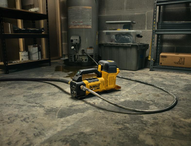 Ferramenta DEWALT DCE050N para fotografia no chão de oficina, ligada à mangueira e cercada por prateleiras.