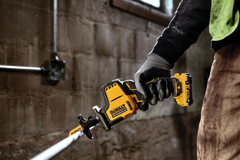 Mão com luva usando serra recíproca sem fio DEWALT DCS312D2 para cortar tubo metálico.
