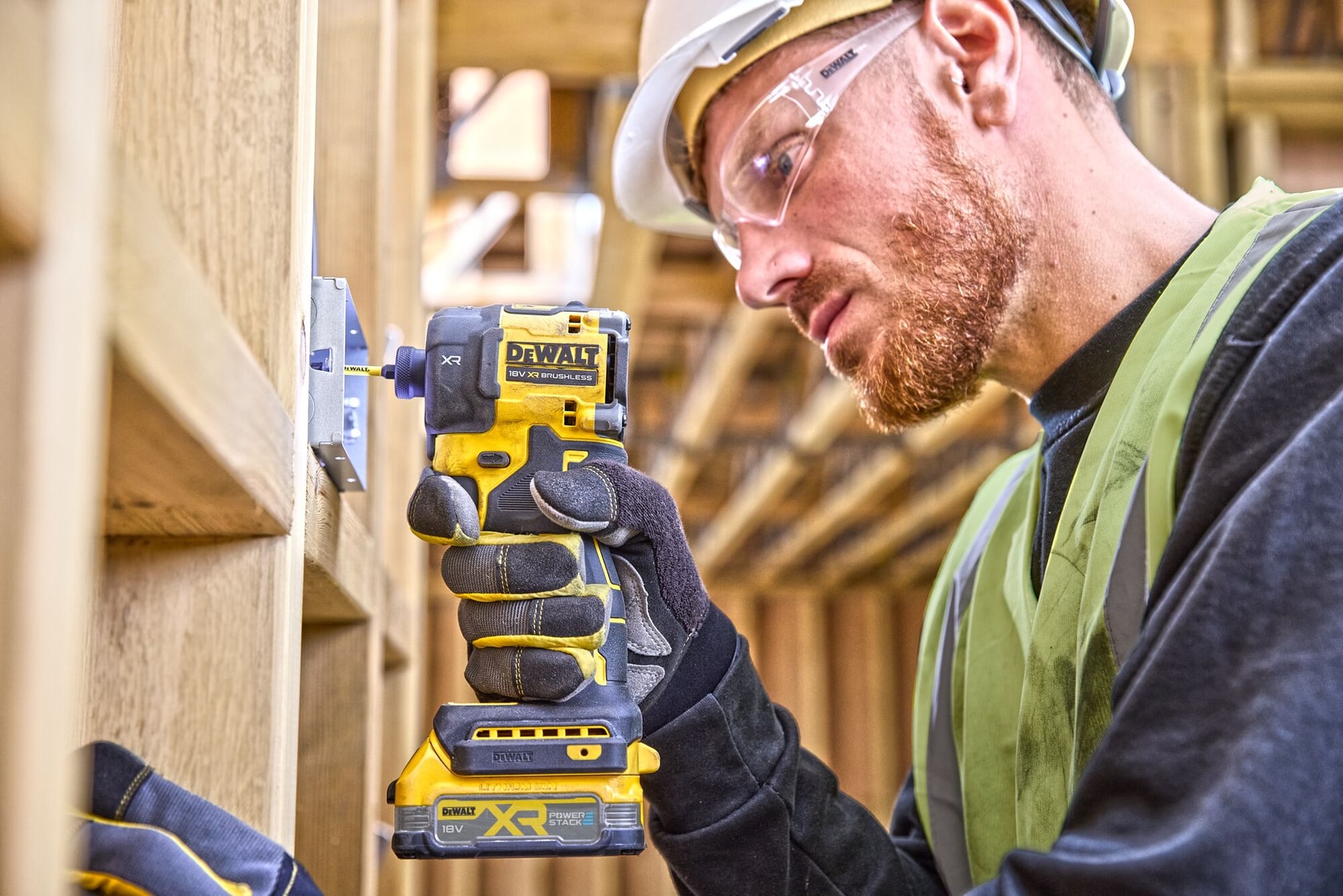 Trabalhador usa um parafusadeira de impacto DEWALT DCF870NT sem fio em estrutura de madeira.